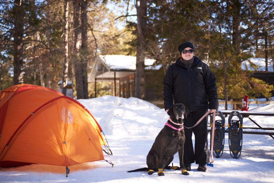Une femme et un chien se tenant à côté d’une tente d’hiver