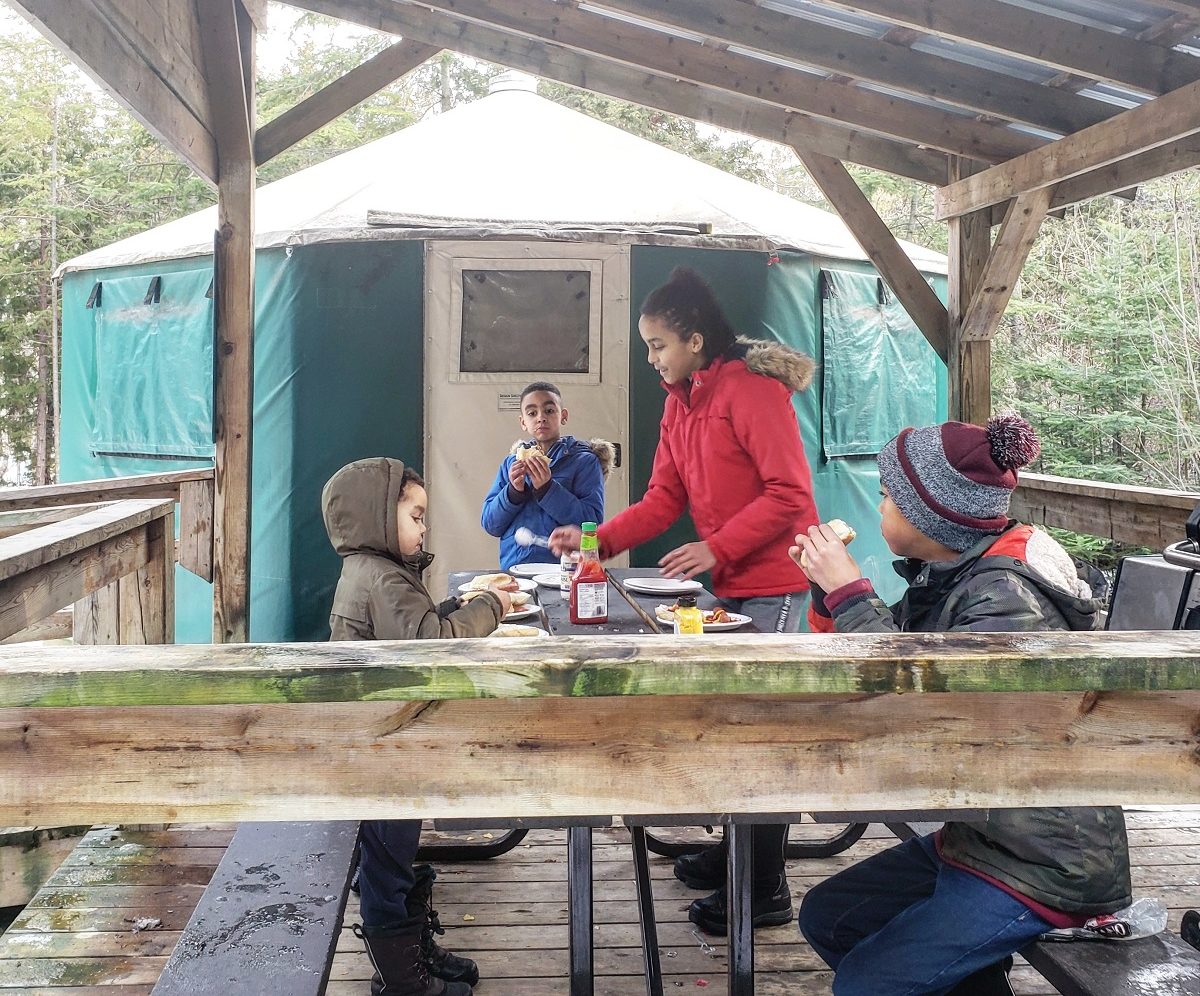 Quatre enfants mangeant à l’extérieur d’une yourte au parc provincial MacGregor Point, en hiver