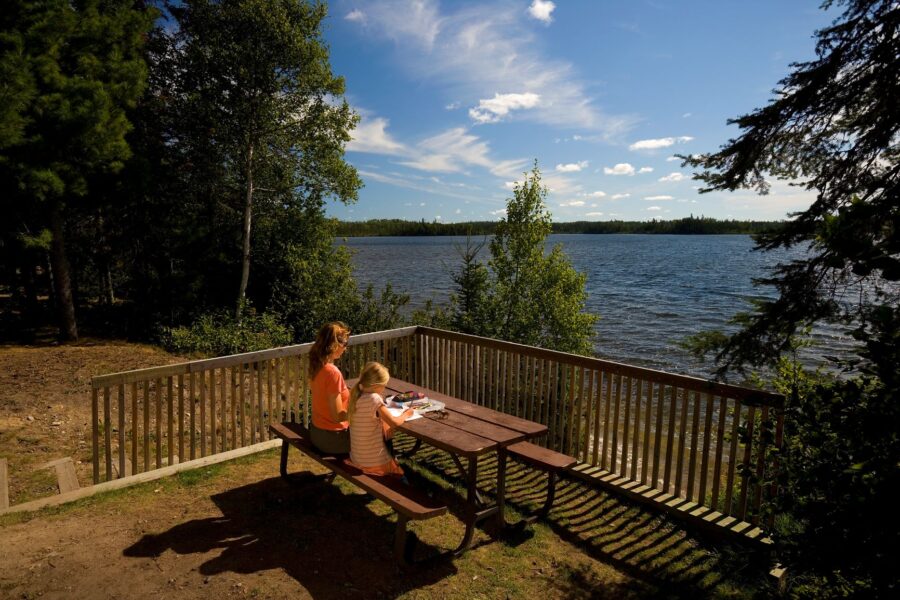 Child and adult sitting at table enjoying view of forest and lake