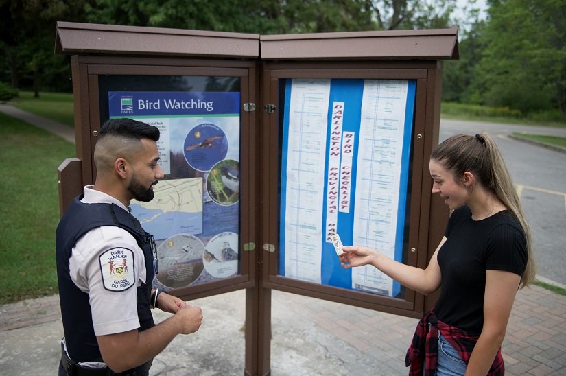 Warden talking to a visitor in front of a sign. 