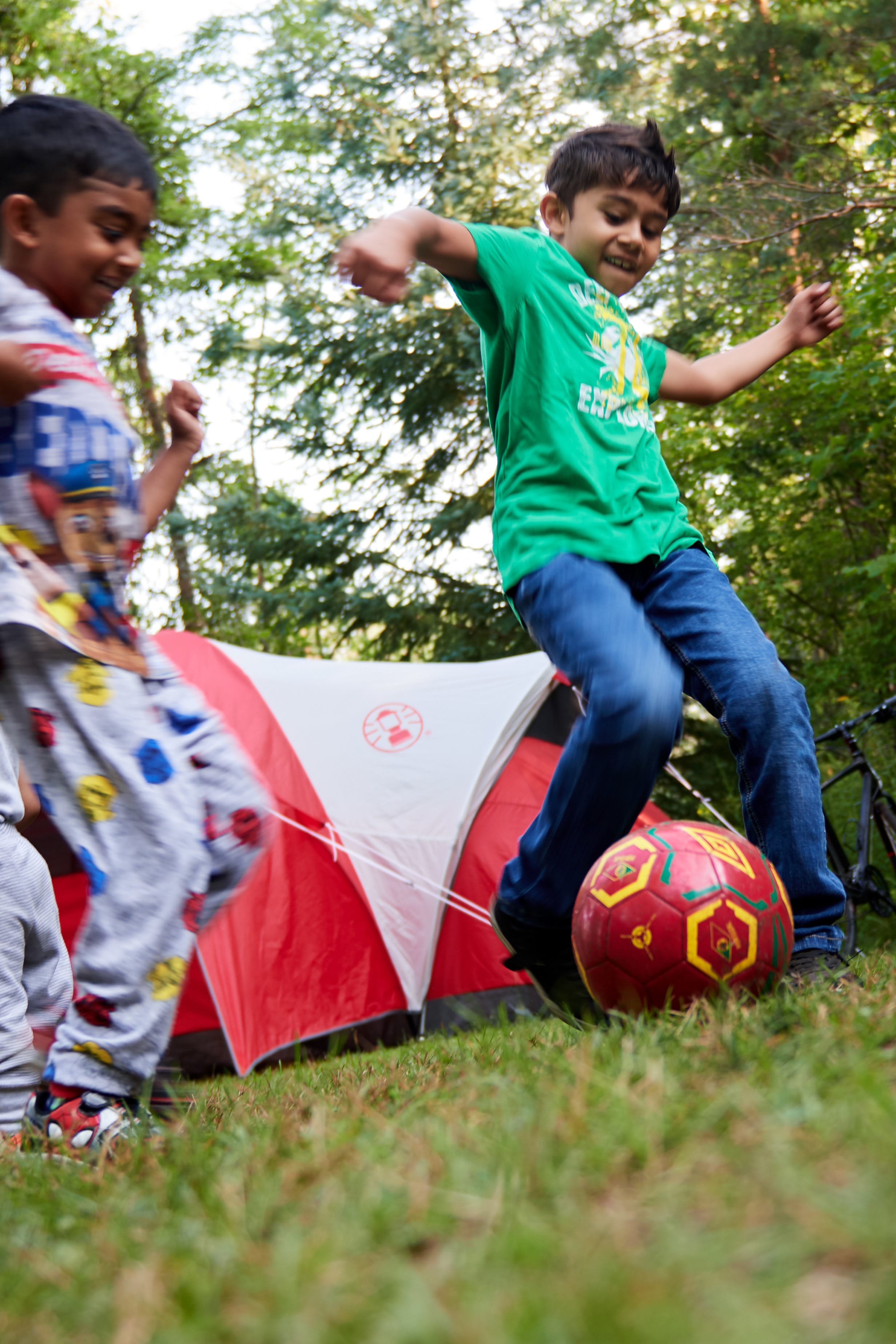 Two young kids play with a soccer ball while camping.