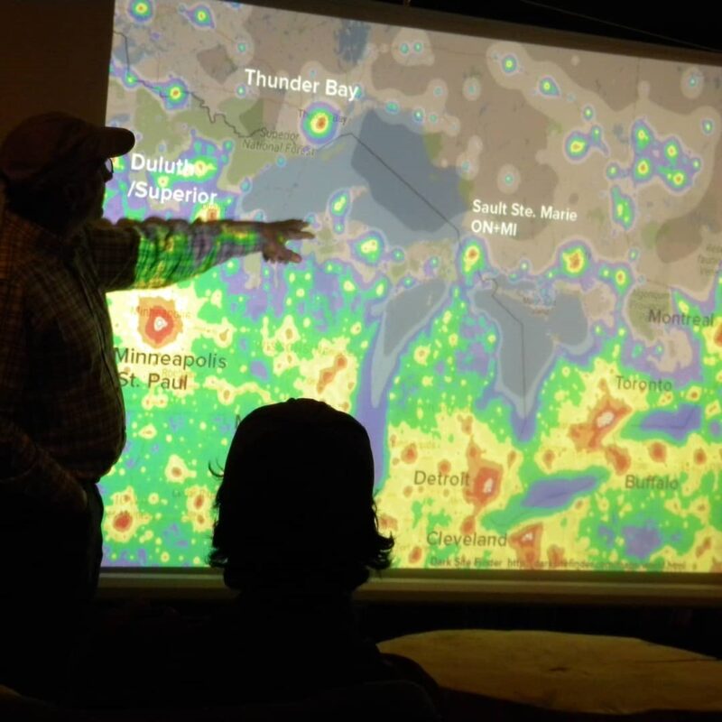 A man pointing to a lit up map on the wall.