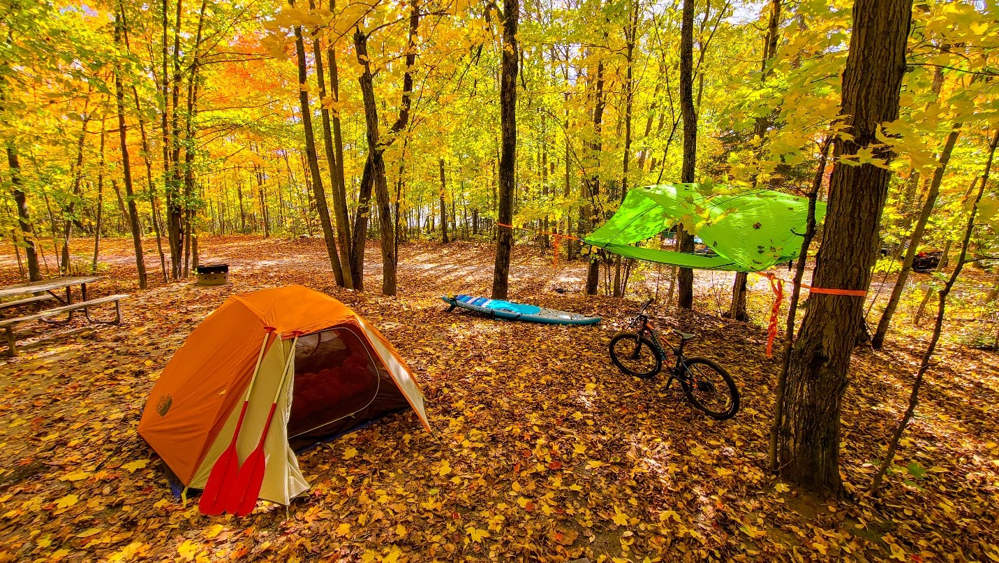 Une tente, une planche à pagaie, un vélo, un hamac, installés sur un emplacement de camping automnal à Restoule.