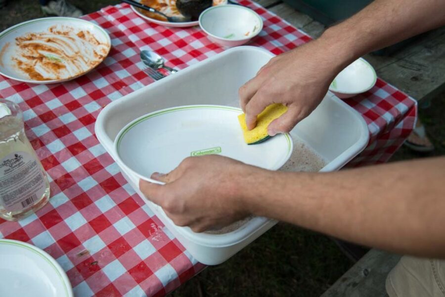 hands washing plate in a basin of water on a picnic table