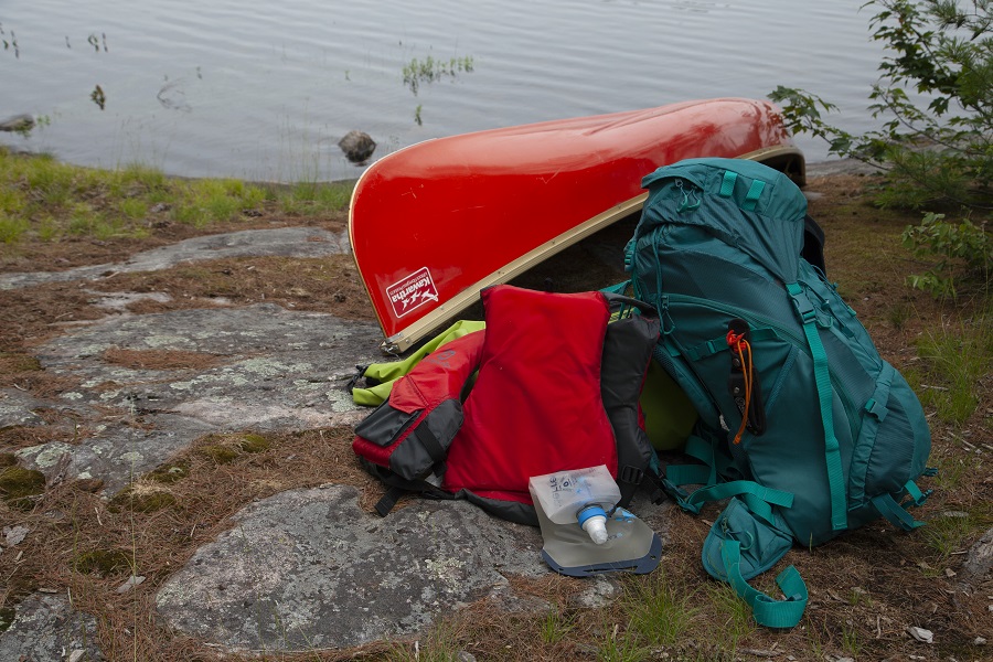 Backcountry gear beside a canoe on the shoreline.