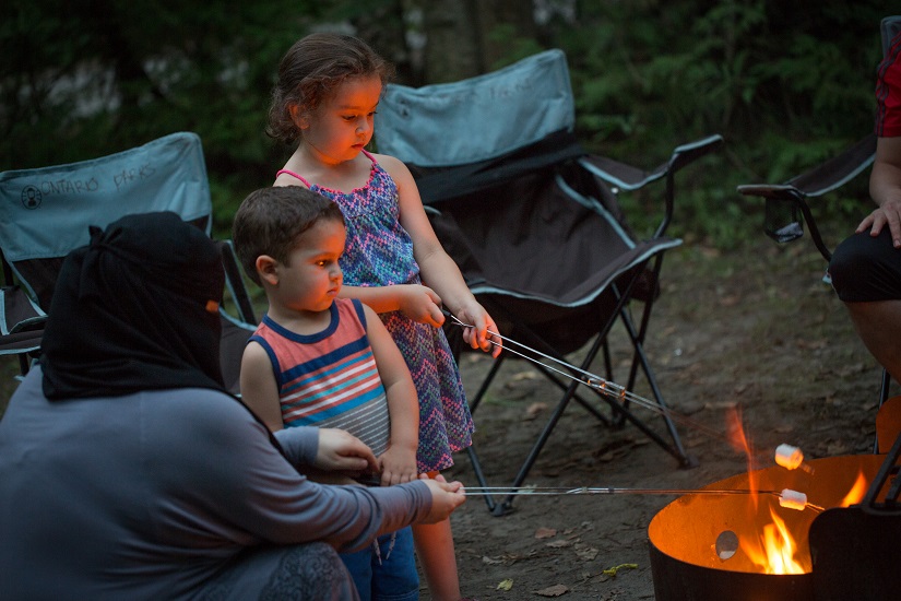 Deux enfants et un parent faisant griller des guimauves.