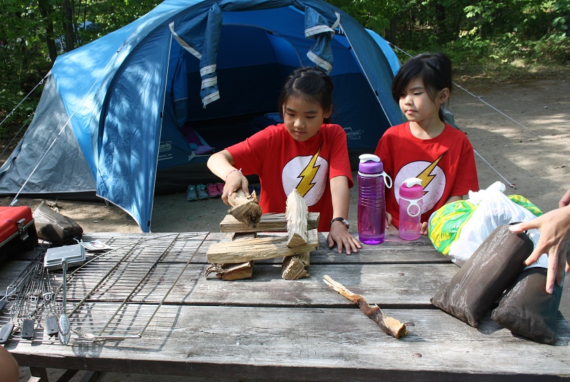 Two children look at firewood on a picnic table.