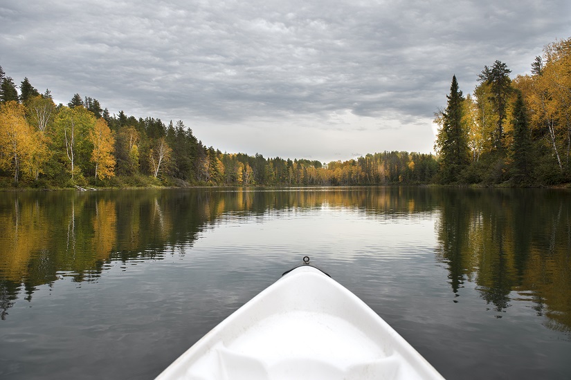 Extrémité d’un kayak sur un lac reflétant les couleurs de l’automne.