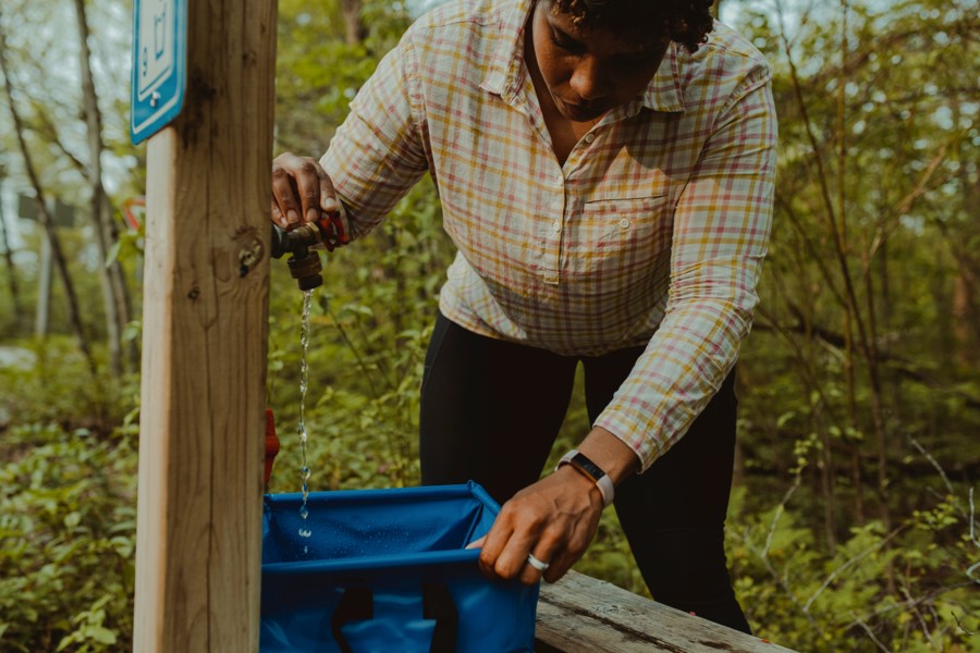 Une femme remplissant une cuve bleue à partir d’un robinet d’eau dans un parc