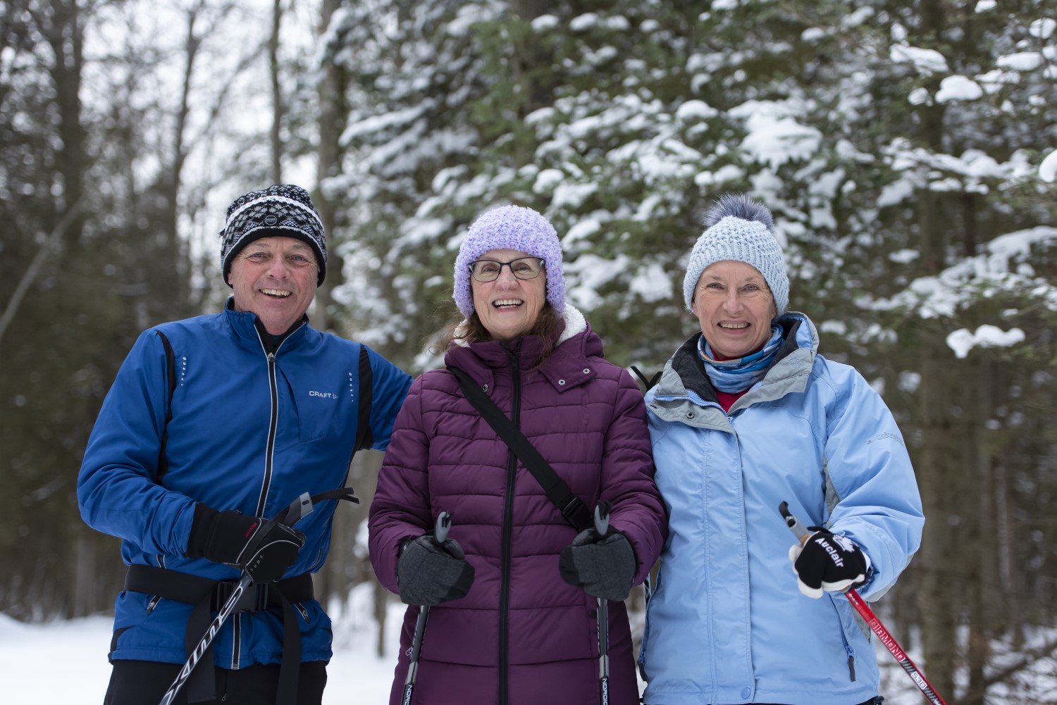 A group of three seniors with cross country skiing gear in a snowy park