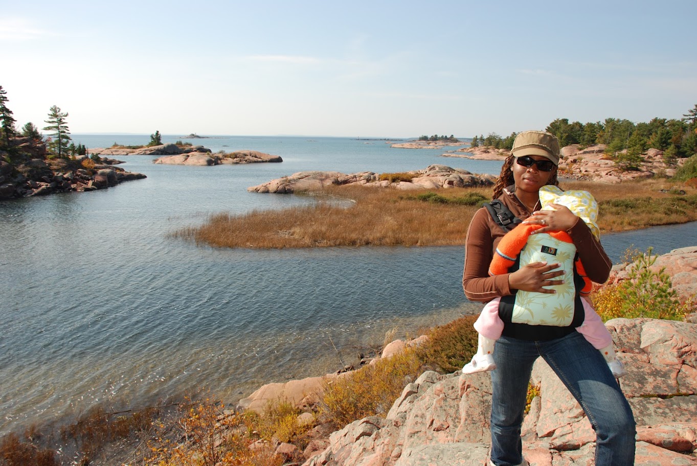 une mère tenant son bébé en écharpe qui regarde un lac