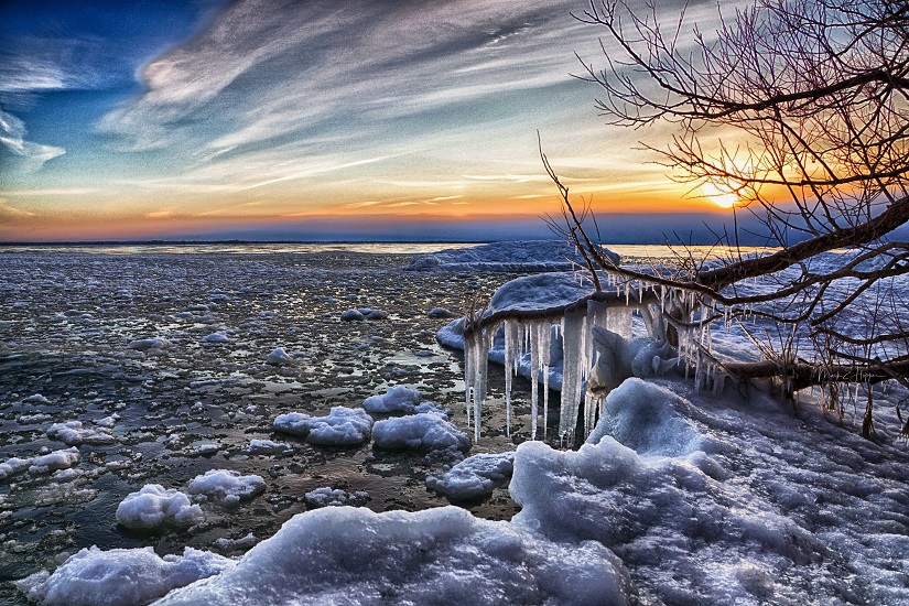 Shoreline covered with ice and snow with sunset in background.