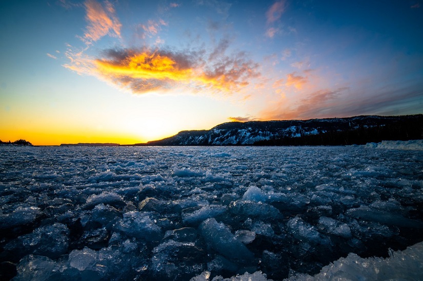 Sunset over froze lake with large cliff in background.