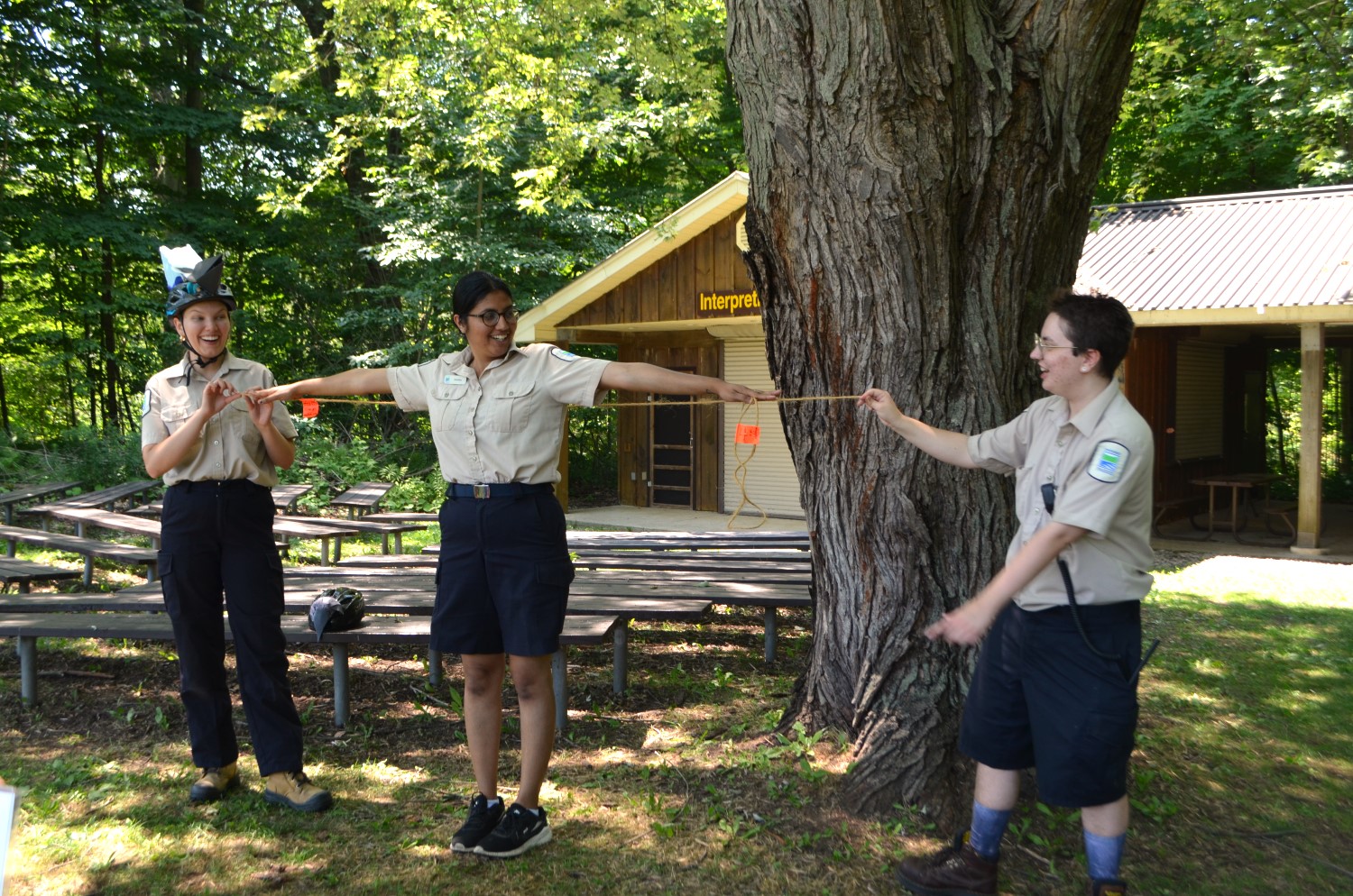 Three Ontario Parks staff standing in a line. The middle person holding their arms out at shoulder height and the other two are using rope to measure her arm span.