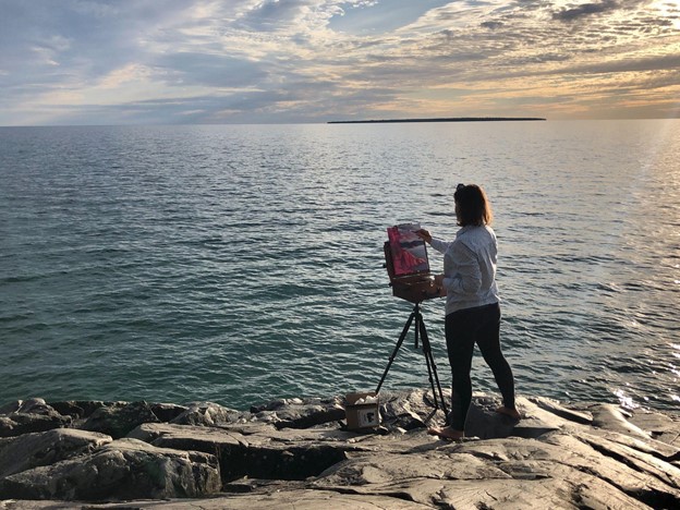 person painting on easel looking out at water