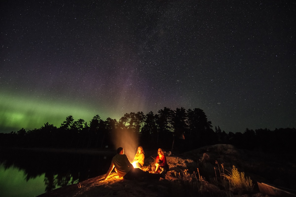 group around a campfire under northern lights