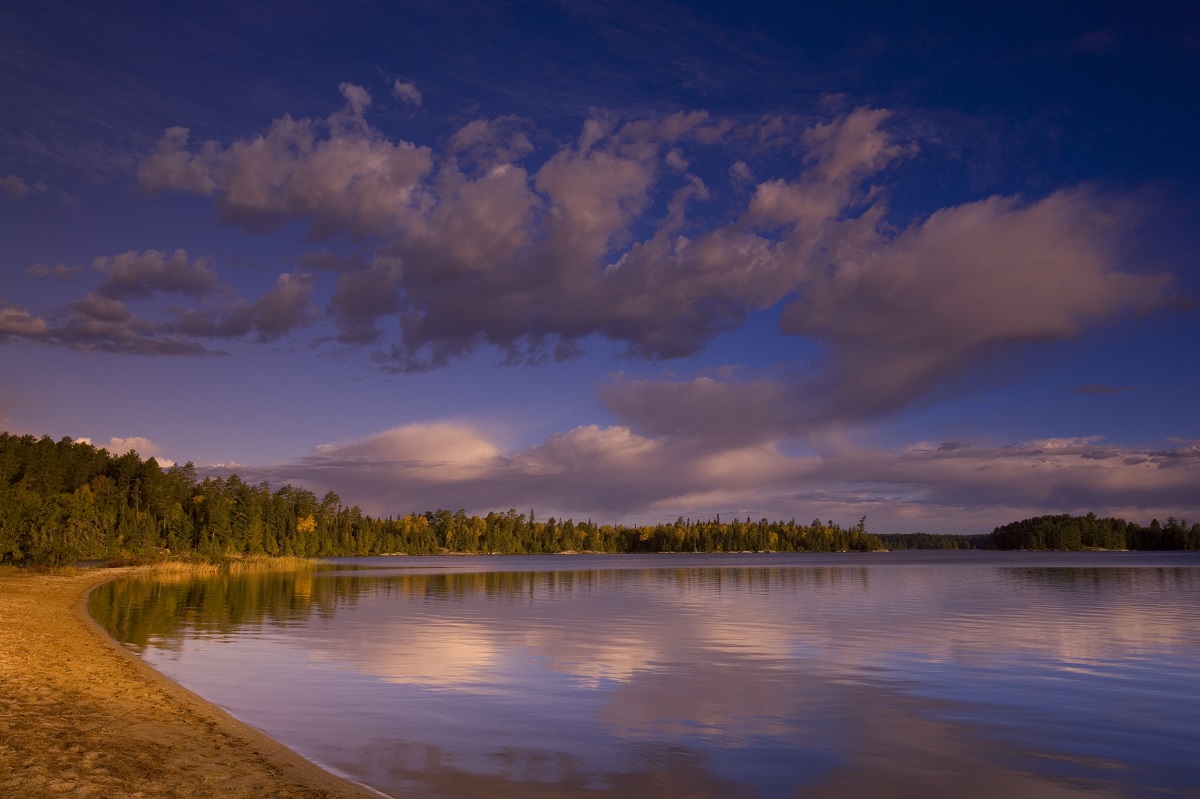 sandy beach by lake with reflections of clouds