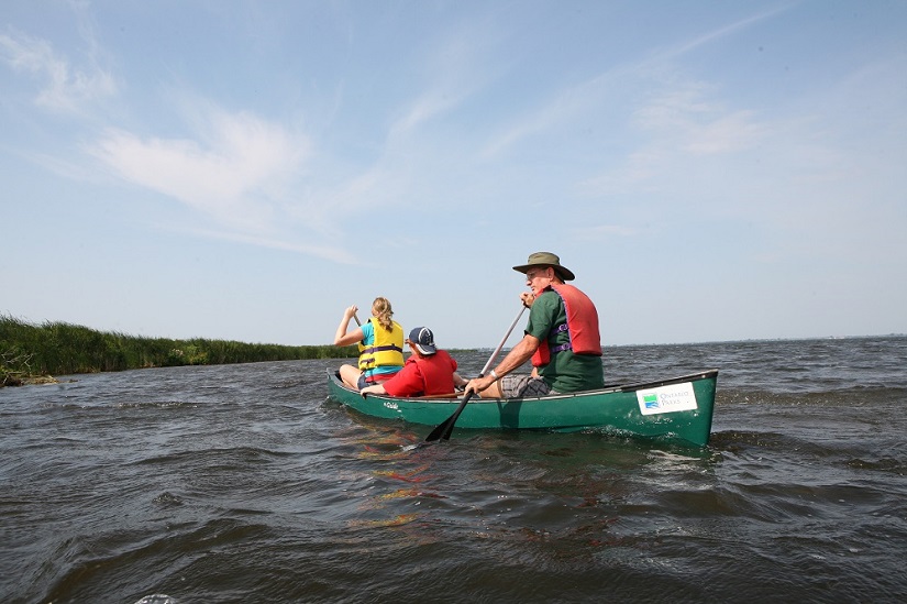 Three paddlers in canoe on lake. 