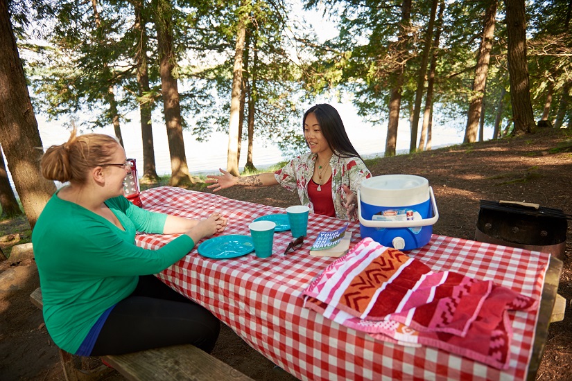 Two campers sitting at picnic table on waterfront site.
