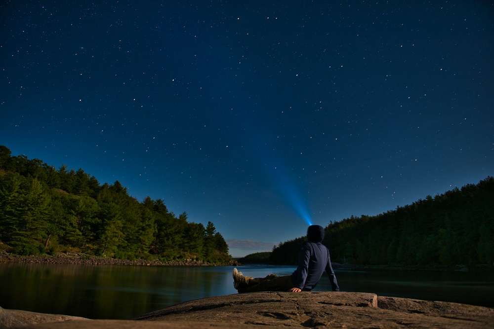 person sitting on shoreline, looking at stars