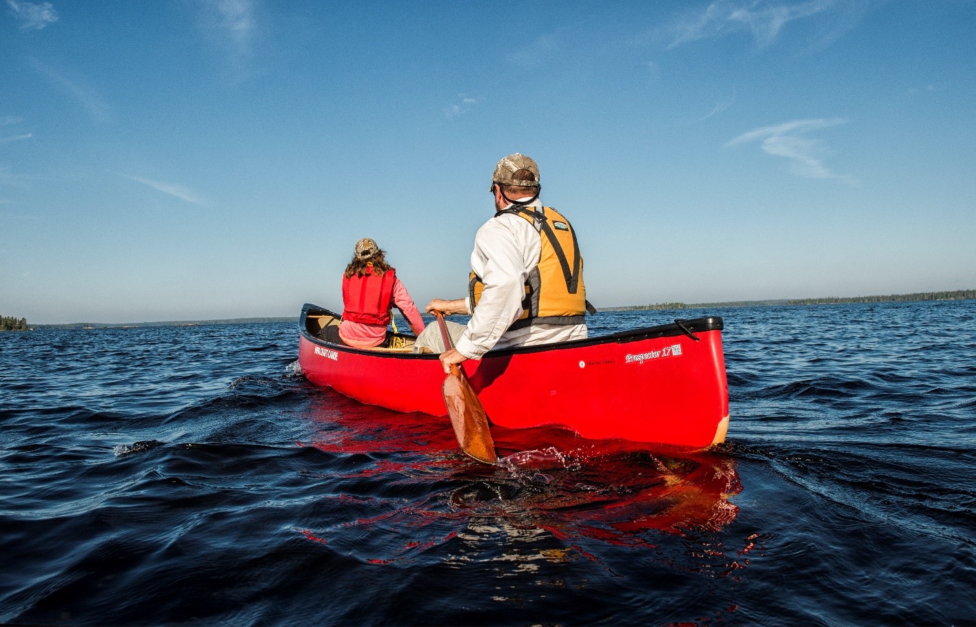 Two people in a red canoe in the open water, paddling away from the camera.