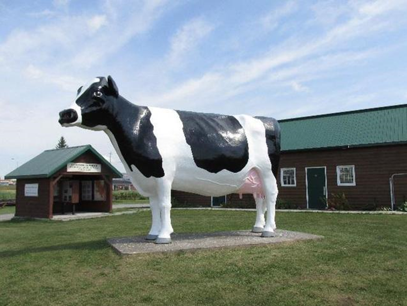 A large black and white cow statue outside of a brown building with a green roof.