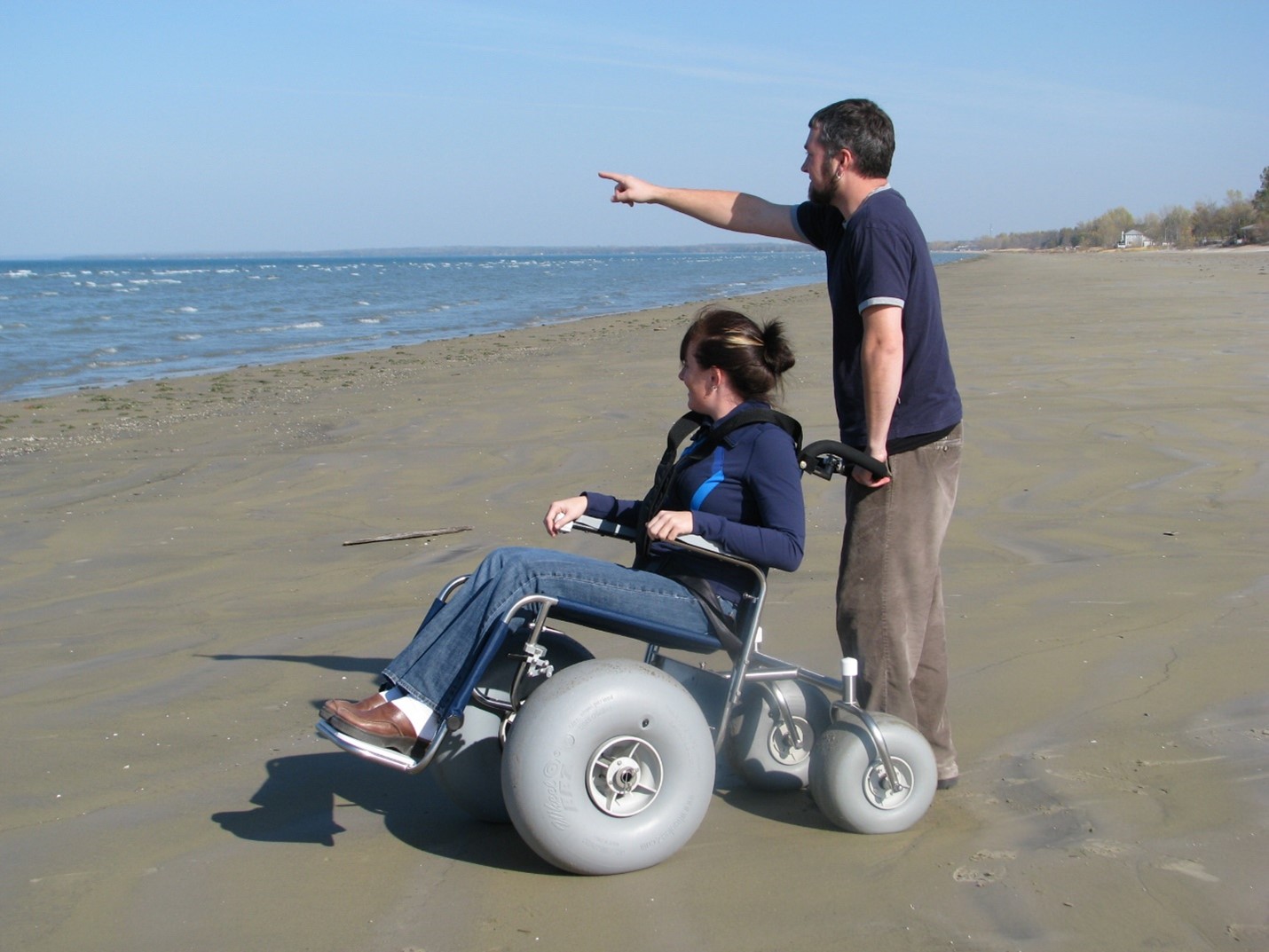 person pushing another on all-terrain wheelchair on beach