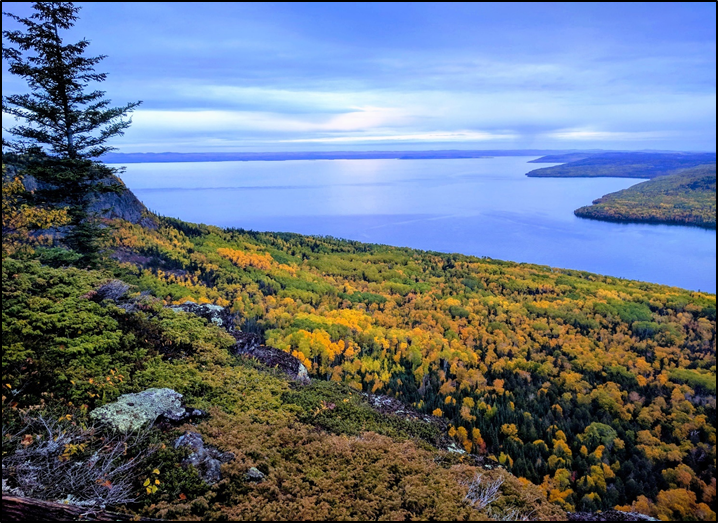 Belvédère rocailleux surplombant une forêt aux couleurs de l’automne et un grand lac.