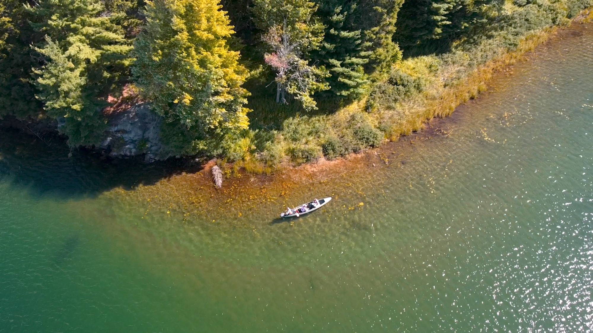 A drone image of a canoe near the edge of a large lake.
