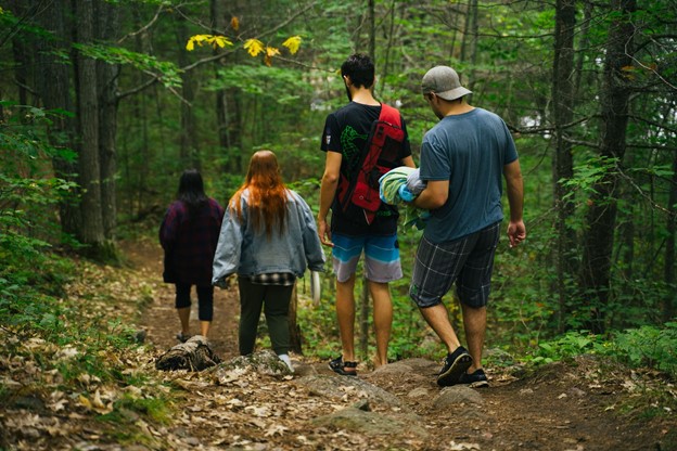Quatre jeunes gens marchant dans une forêt, dos à la caméra.
