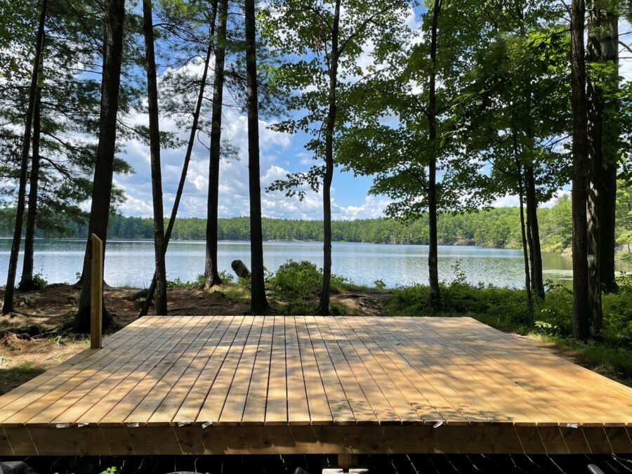 A square wooden platform in a wooded area next to a large lake.