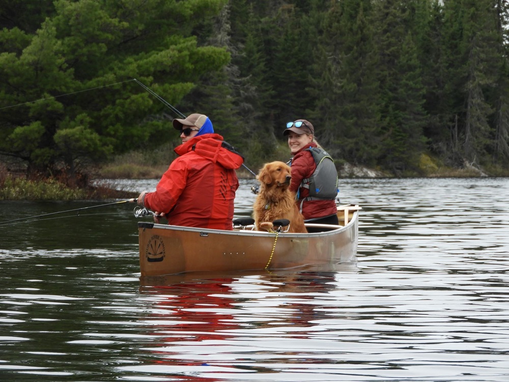 two people fishing from canoe with dog