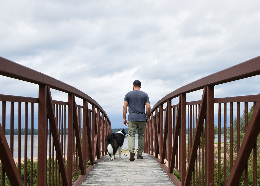 Dog and man hiking over bridge.