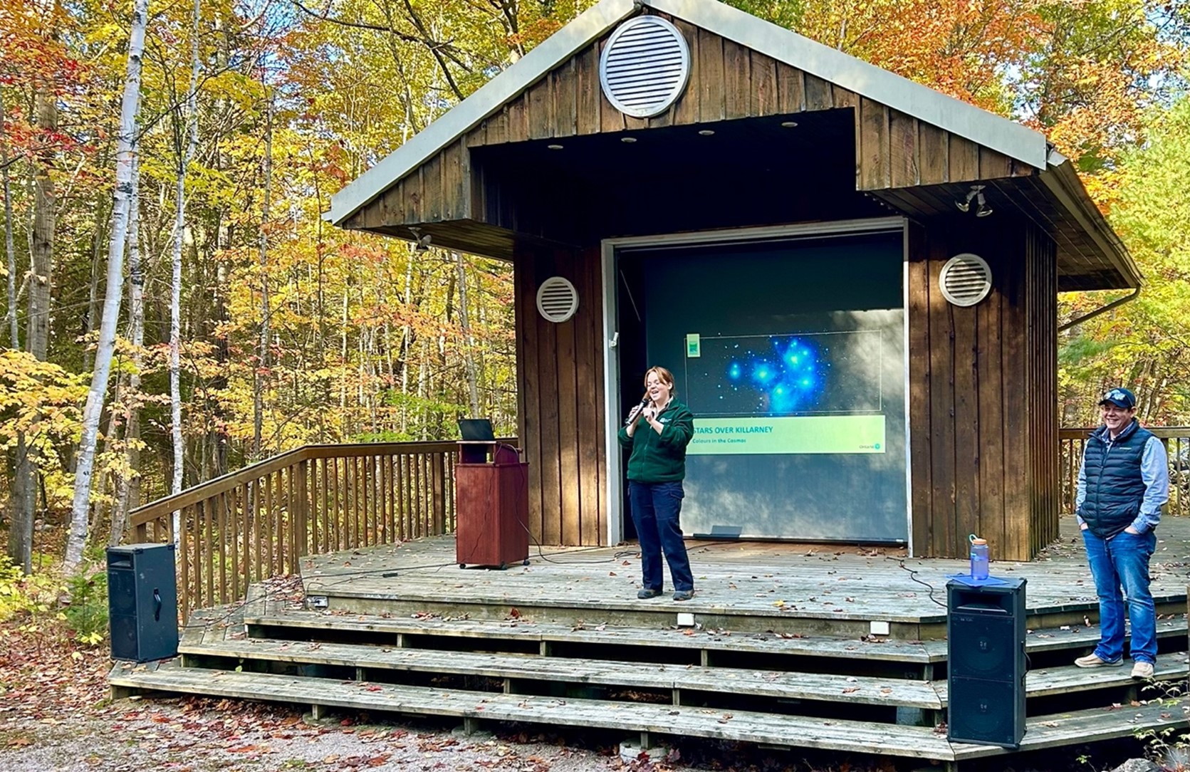 staff standing at outdoor amphitheater, presentation playing on screen