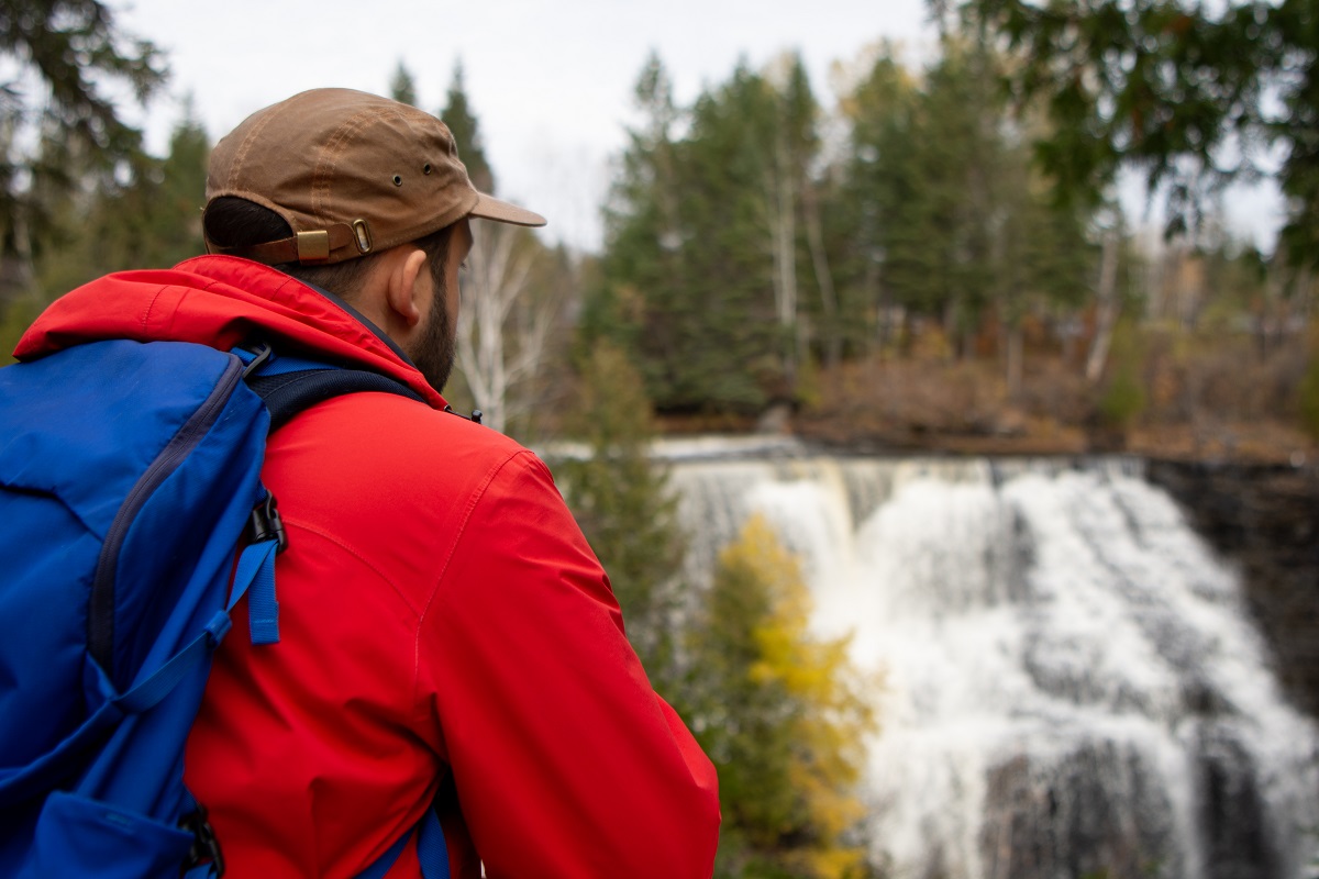 man with red coat and backpack looking over waterfall