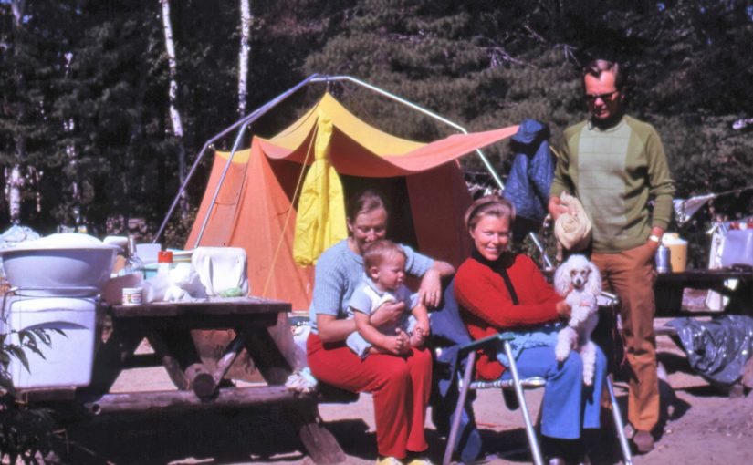 Famille assise posant pour la photo sur un emplacement de camping dans les années 1970, avec une grande tente orange en arrière-plan