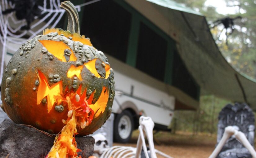 Emplacement de camping décoré pour l’Halloween avec une citrouille devant la tente-roulotte