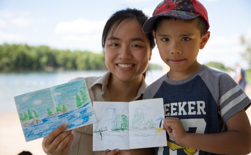 Une employée de Parcs Ontario tient son croquis au crayon de couleur à côté d'un jeune enfant qui tient son œuvre d'art.