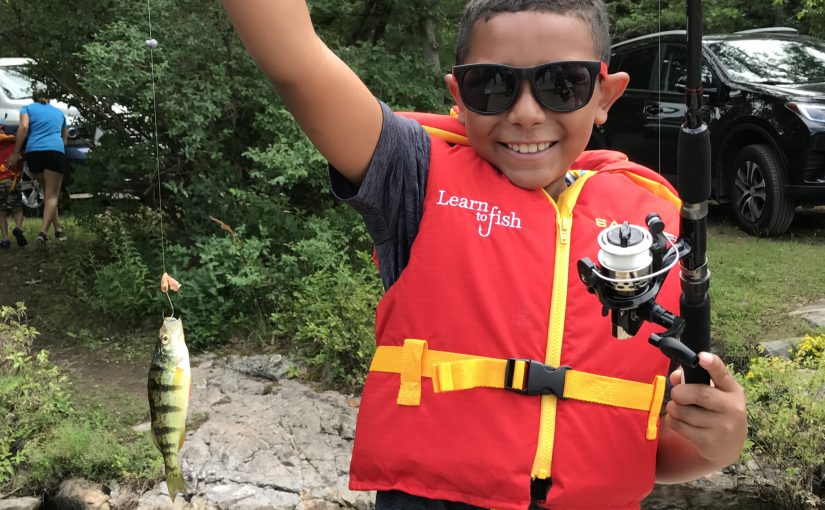 Child with lifejacket holds up yellow perch