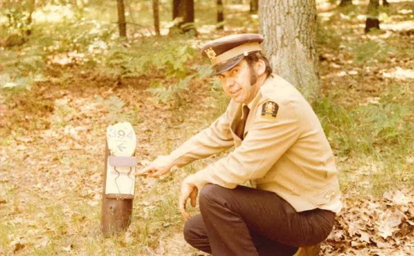 Park warden from the 80's crouches beside a site permit and holder