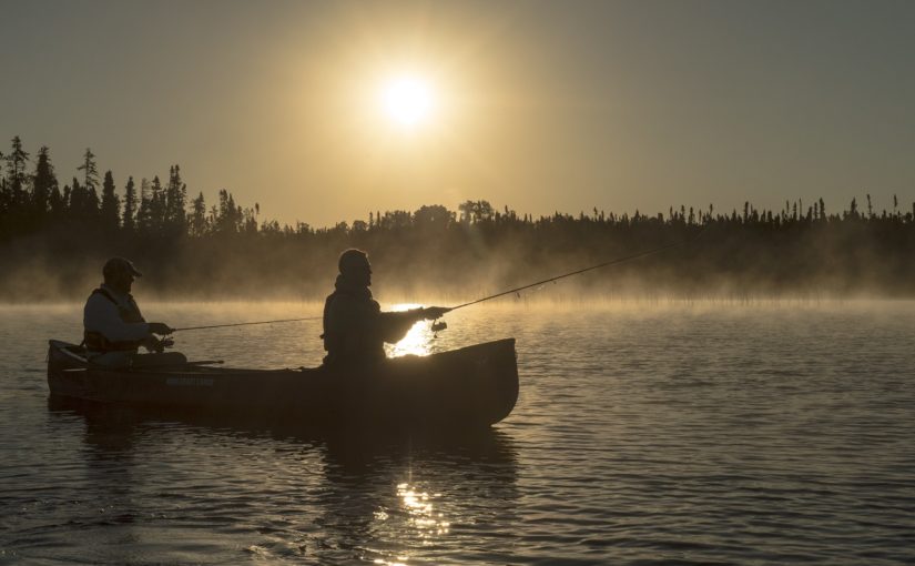 Two people fishing at sunset with mist rising off the lake and boreal forest in the background