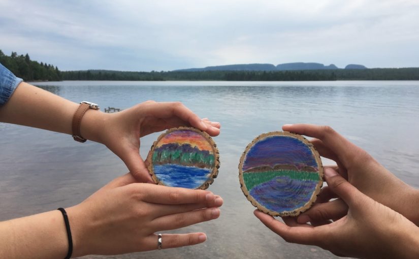 Two painted tree cookies held up in the foreground of the Sleeping Giant