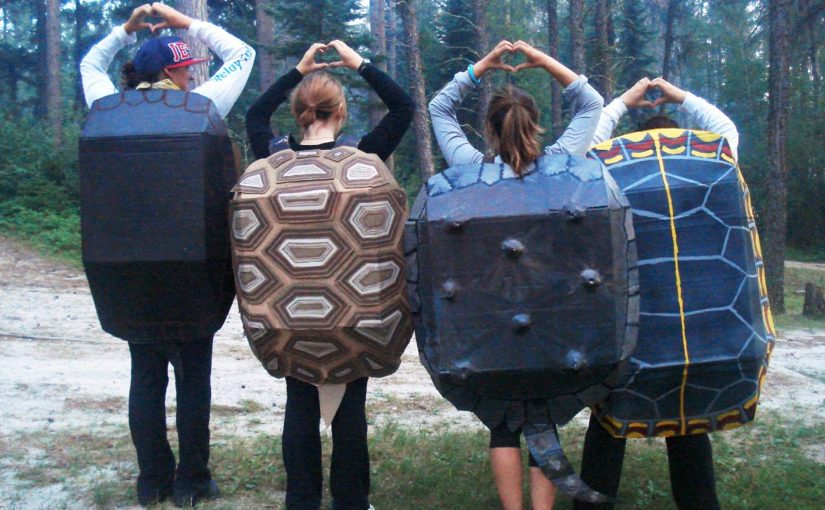Four people lined up with turtle shells on their backs