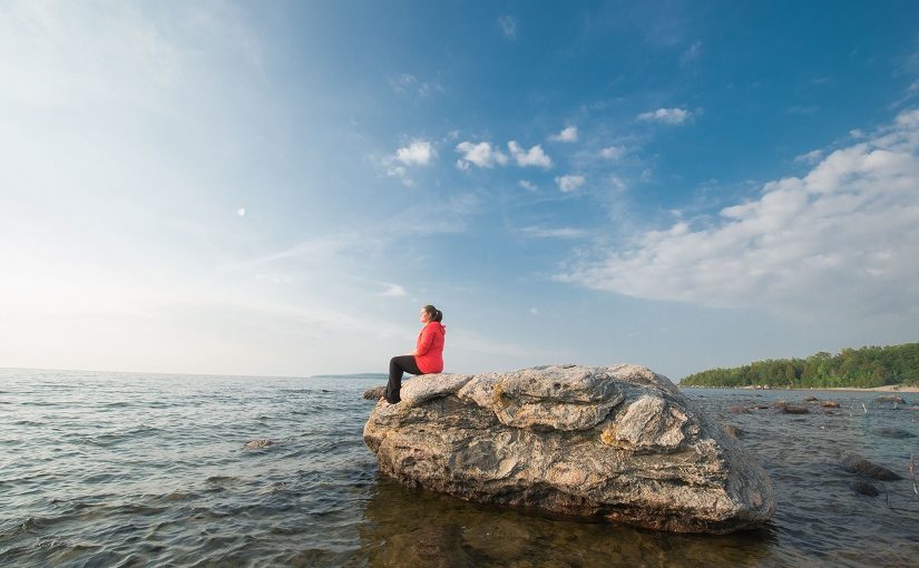 Woman sits on rock in lake