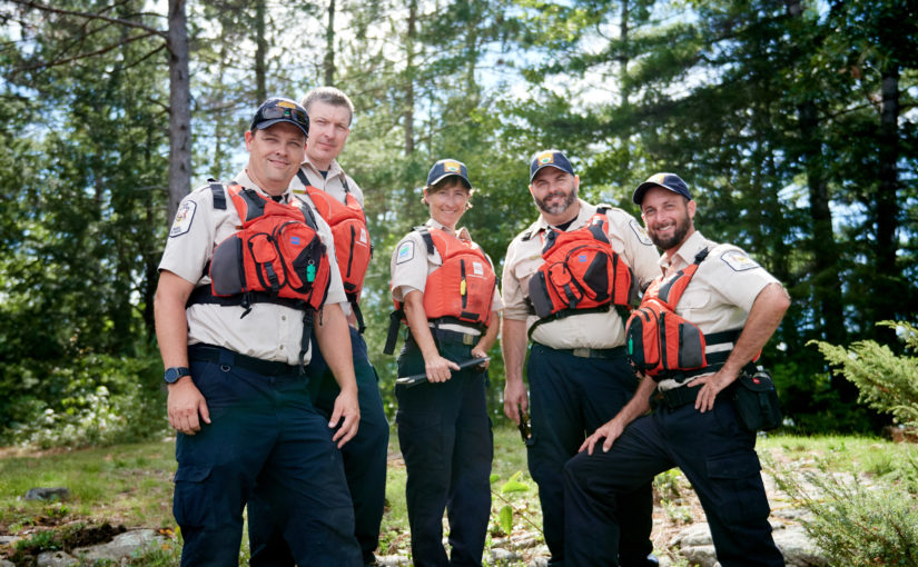 Five smiling park staff in uniform wearing life jackets.