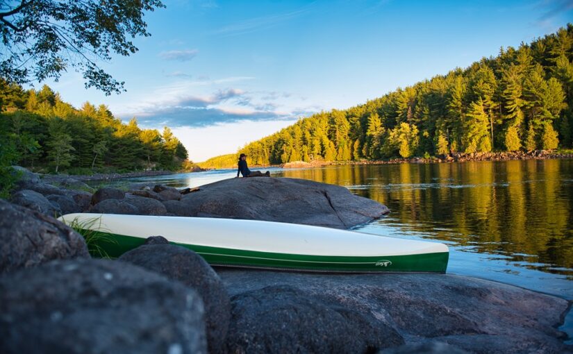 person sitting near canoe on river shore