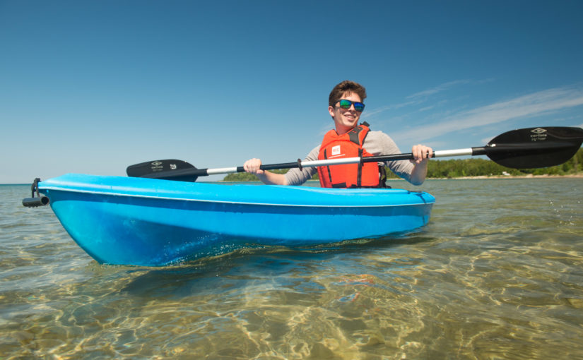 Man in a blue kayak on clear water wearing a PFD.