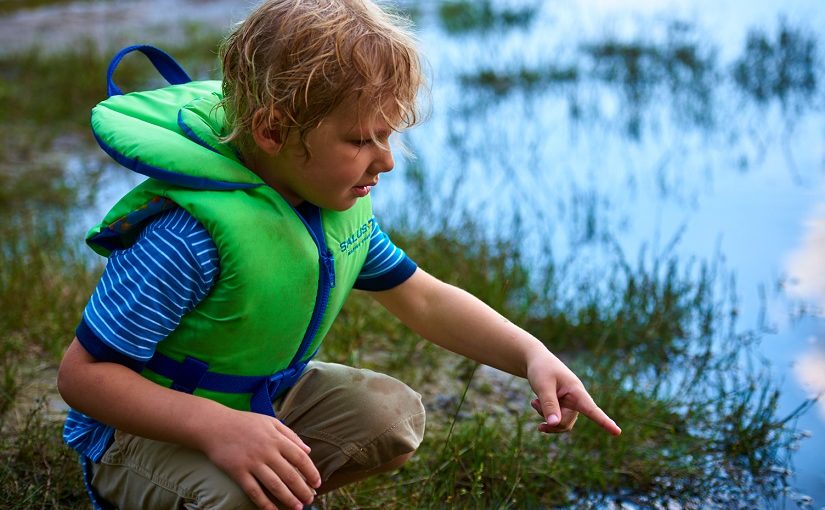 Child examines something in wetland in lifejacket
