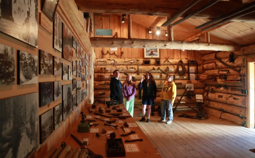 A group of people touring a logging exhibit inside a log building