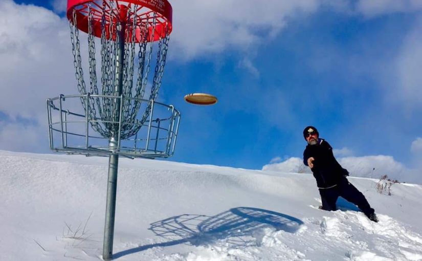 park staff throwing disc on snowy course